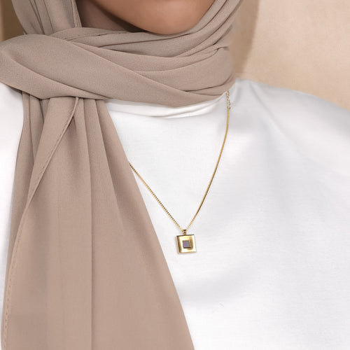 Keepsake open square pendant worn with a white top and beige scarf