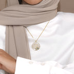 Rooted tree pendant worn over a white shirt and beige scarf